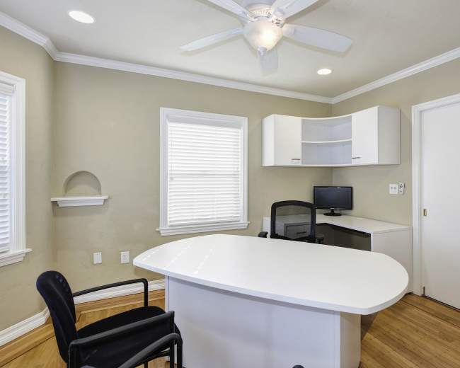 A neatly organized office space with a white desk, a black chair, a computer monitor, and natural light coming through the window.