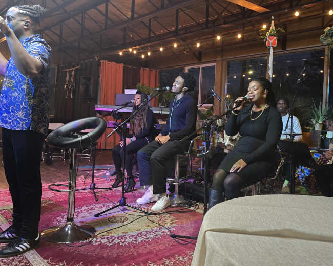 A group of musicians performs on stage in a dimly lit venue, surrounded by instruments and vibrant decor.