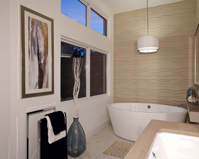 The image shows a modern bathroom featuring a freestanding tub, a stone countertop vanity, large windows, and decorative elements like a vase and framed artwork.