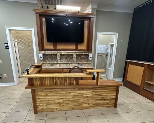 A modern reception area with a wooden reception desk, a large flat-screen TV mounted above it, and tiled flooring.