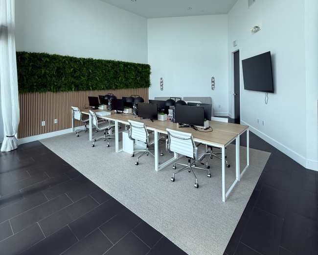 The image shows a modern office space featuring a row of desks with computer monitors, white ergonomic chairs, and a vertical green wall.
