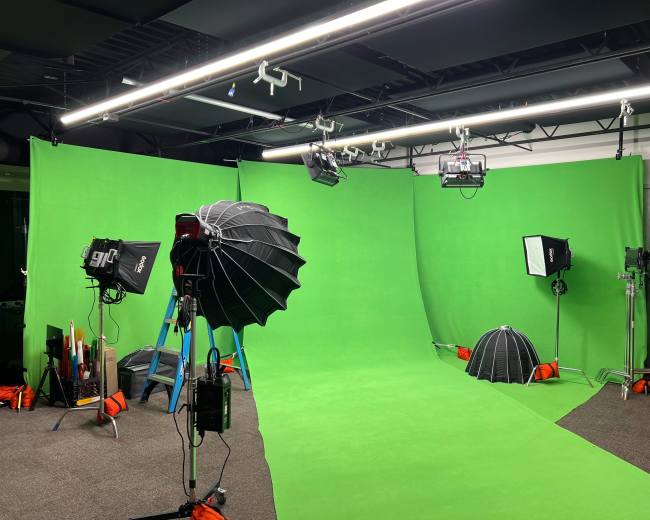 A film studio setup with green backgrounds, lighting equipment, and a ladder positioned in the center.