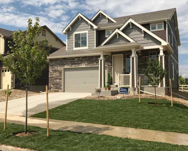 A two-story house with stone and siding exterior features a front porch, garage, and freshly landscaped lawn with young trees.