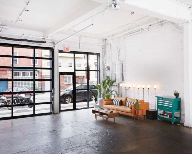 The image shows a bright, modern interior of a commercial space with a large glass door, a sofa, and a row of light fixtures.