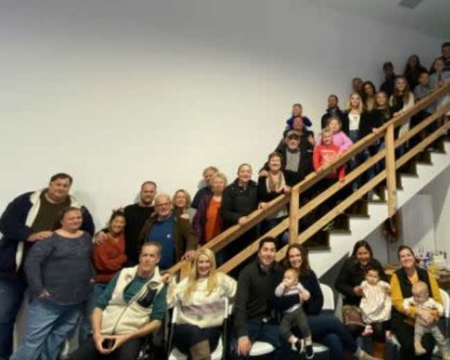 A large group of people of varying ages poses together on and around a staircase in a well-lit indoor space.