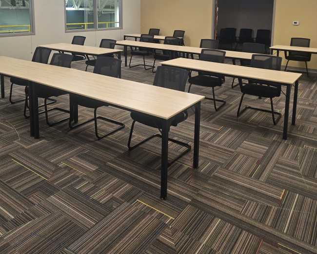 The image shows a modern classroom with several rows of tables and chairs arranged in a spacious, well-lit environment.