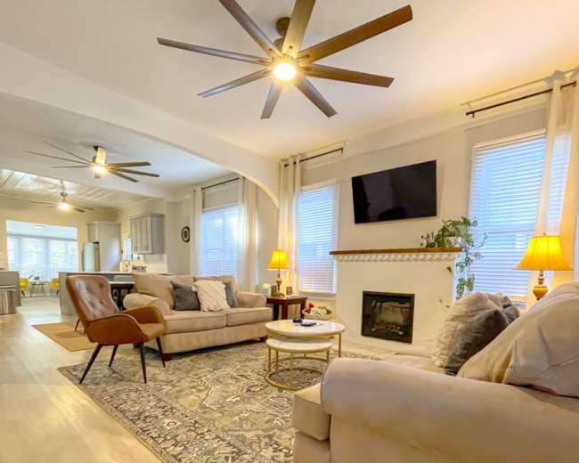 The living room features two sofas, a coffee table, and a fireplace, with large windows allowing natural light to fill the space.