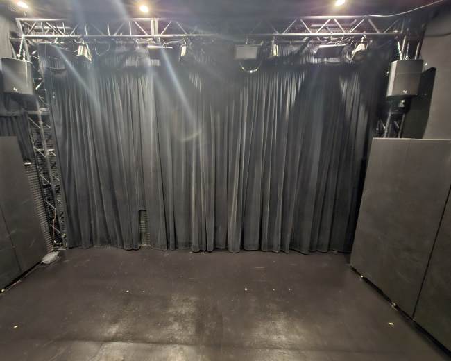 A stage area with black curtains and sound equipment mounted on the walls.