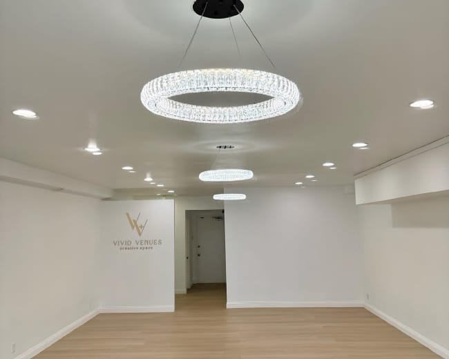 The image shows a spacious, empty room featuring two circular crystal chandeliers and a wall with the text "Vivid Venues."