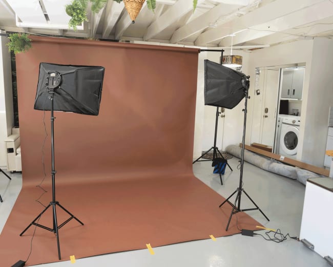 A photography studio setup with two softbox lights positioned on either side of a brown backdrop.