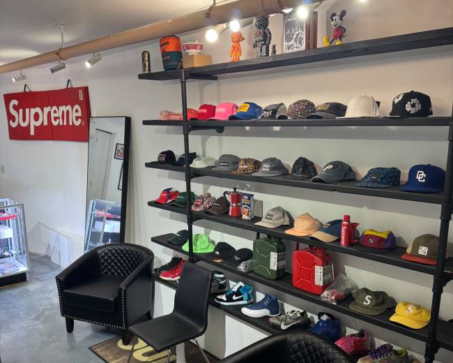 The image shows a retail space with shelves displaying various hats and accessories, along with a seating area featuring two black chairs.
