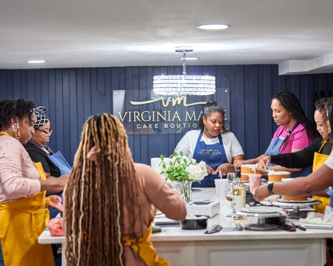 A group of women work together around a kitchen island, carefully decorating cakes in a cake boutique.
