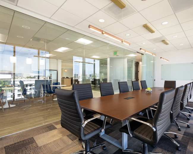 A large conference room features a wooden table surrounded by ergonomic black chairs, with glass walls revealing an adjacent workspace.