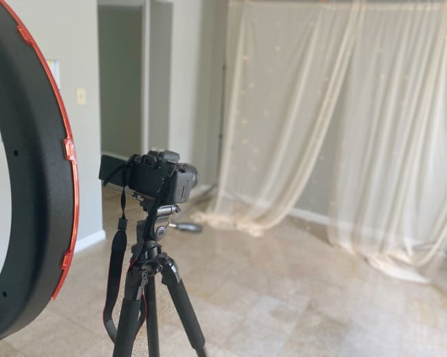 A camera on a tripod is set up facing a fabric backdrop with lights, ready for a photoshoot.
