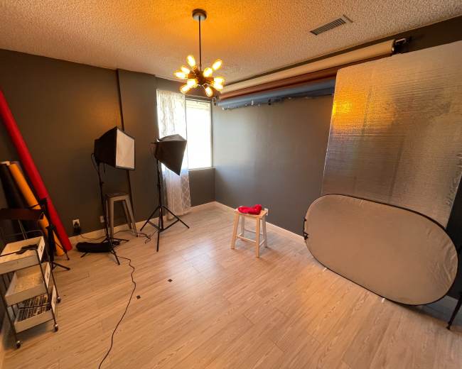 A well-lit photography studio with a backdrop setup, a stool, and two softbox lights.