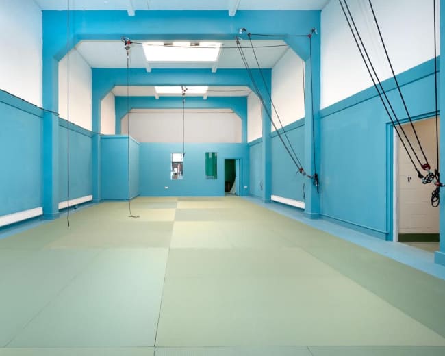The image shows a spacious room with blue walls and a green mat covering the floor, equipped with overhead pulleys and cables.