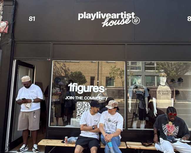 The image shows a storefront labeled "playliveartisthouse," with three individuals sitting on a bench outside and a fourth person standing nearby, all in urban clothing.