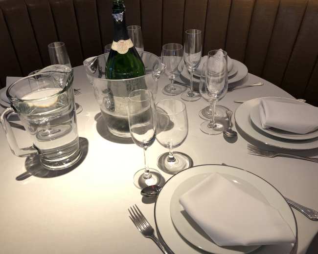 A dining table is set with multiple glassware, a bottle of champagne in an ice bucket, and neatly arranged plates and utensils.