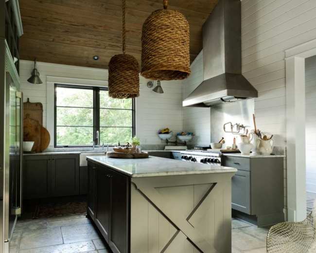 The image shows a modern kitchen with a central island, gray cabinetry, a stainless steel range hood, and large woven pendant lights.