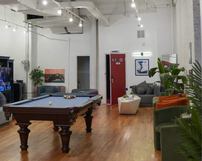 The image shows a spacious lounge area featuring a pool table, various seating arrangements, and decorative wall art.