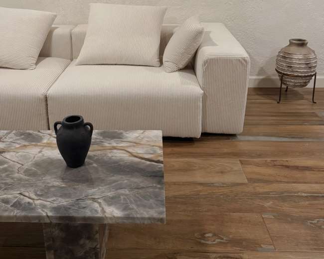 A light-colored sofa with striped cushions is positioned next to a marble coffee table and a decorative vase on the table in a minimalist room.