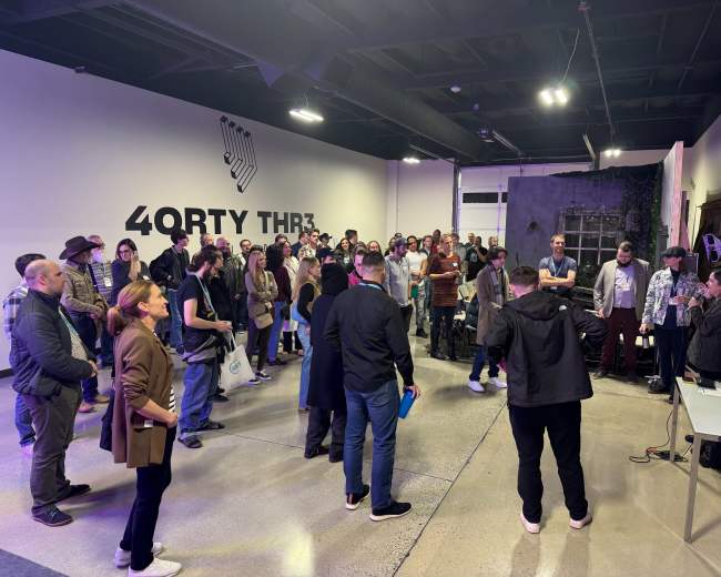 A crowd of people gathers in a brightly lit indoor space for an event, with some individuals standing in front of a presentation area.
