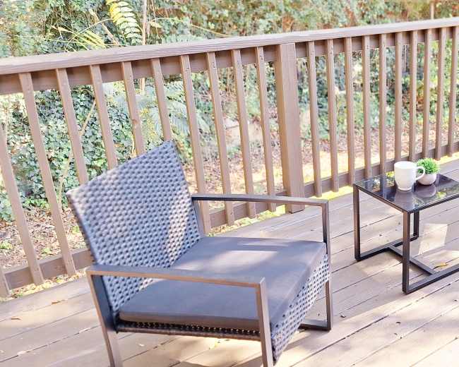 A small deck features two chairs and a coffee table adorned with plants.