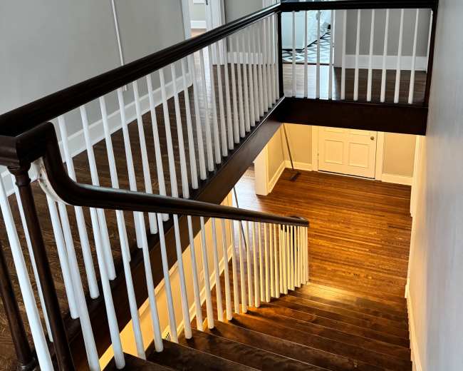 The image shows a wooden staircase with a banister leading down to a lower level, illuminated by warm light at the bottom.