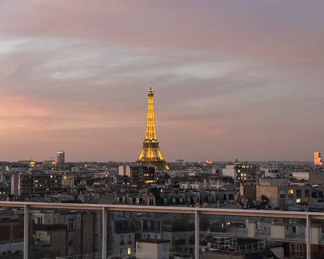 The image shows a cityscape of Paris at dusk, featuring the illuminated Eiffel Tower in the distance against a colorful sky.