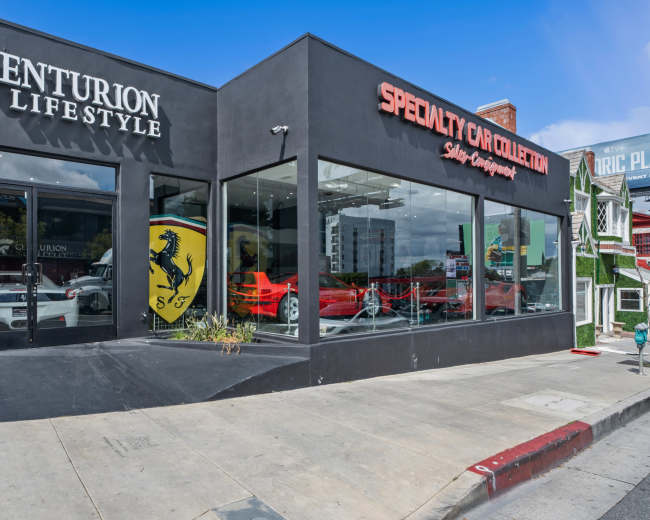 The image shows a storefront featuring a luxury car showroom with a red Ferrari displayed in the window alongside the branding of "Centurion Lifestyle" and "Specialty Car Collection."