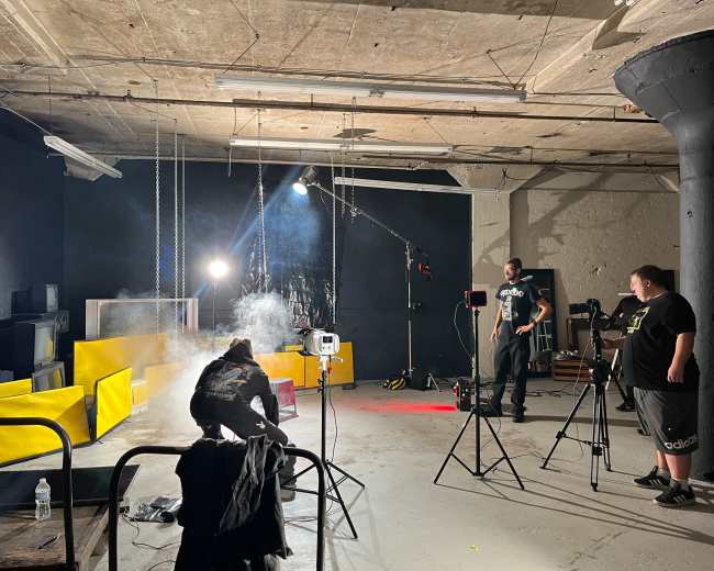 A group of people is setting up a photo shoot in an industrial room with yellow furniture and various lighting equipment.