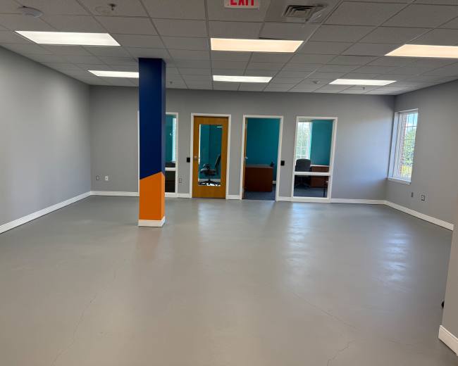 An empty office space features grey floors, blue and orange accent walls, and multiple glass-paneled rooms.