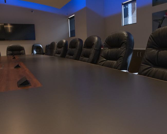 A long conference table with several black leather chairs arranged along its sides in a brightly lit meeting room.