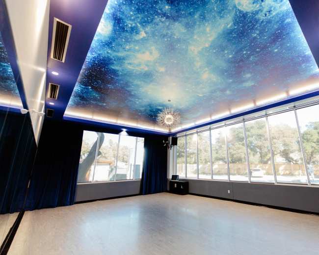 A spacious room with a starry ceiling mural and large windows allowing natural light to enter.