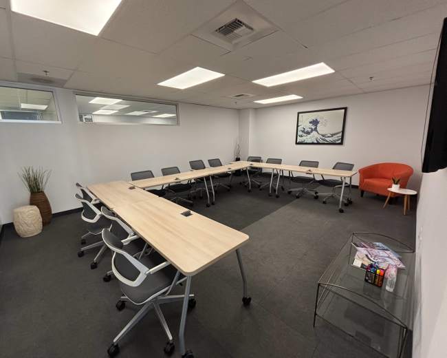 The image shows a modern conference room arranged with multiple tables and chairs, featuring a minimalist design and a large wall art piece.
