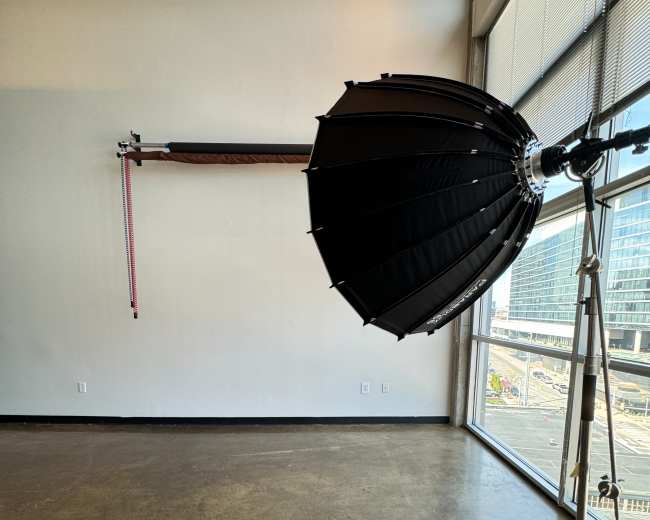 A photography studio with a large softbox light on a stand and a wall-mounted backdrop support system.
