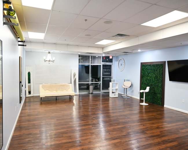 A spacious, well-lit room with hardwood flooring, featuring a seating area, a large mirror, and a decorative green wall.