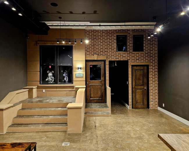 The image shows a modern interior featuring a brick wall, a set of steps leading up to a window with decorative elements, and two doors on the right side of the scene.