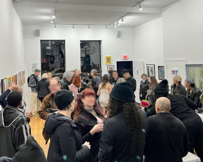 A crowded art gallery features guests mingling and viewing various artworks displayed along the walls.