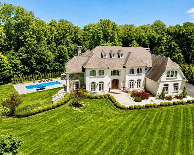 The image shows a large, two-story house with a manicured lawn and a swimming pool in the backyard, surrounded by trees.