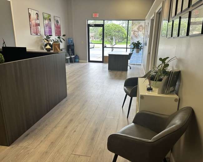 The image shows a modern office reception area with a desk, chairs, and large windows that provide natural light.