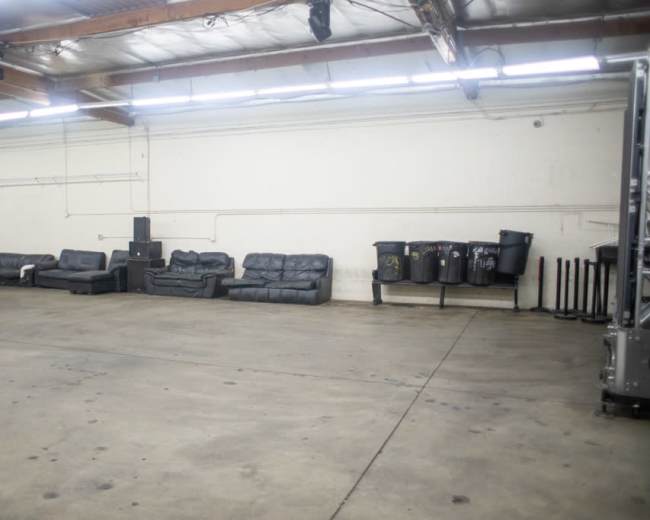 The image shows a spacious indoor area with several black couches lined against a wall and trash bins placed nearby.