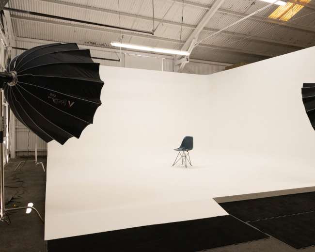 A single blue chair is positioned in the center of a photography studio with large softbox lights on either side.