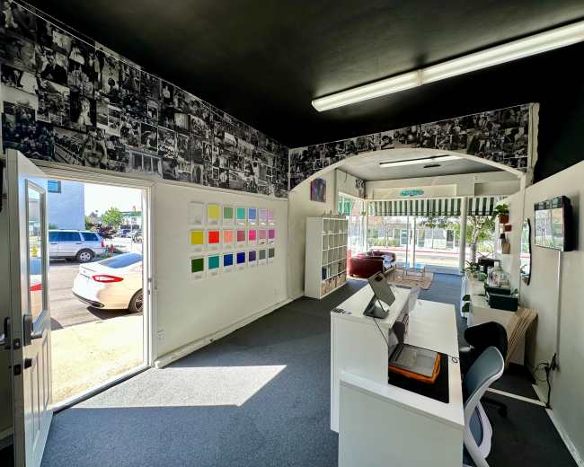 The image shows an interior view of a brightly lit office space with a counter, shelves, and a wall decorated with black-and-white photographs.