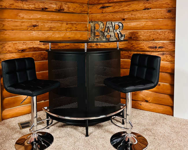 The image shows a small coffee bar with two black bar stools in a wooden-paneled room.
