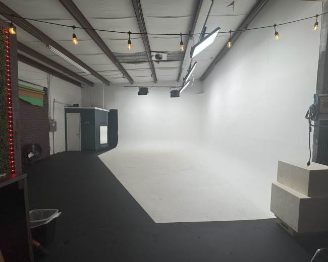 The image shows a spacious studio with a white backdrop, a black floor, and overhead string lights.