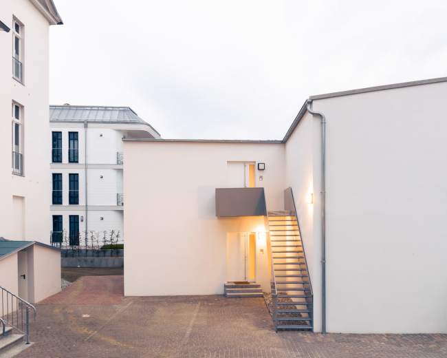 A modern building with a stairway leading to an upper entrance, surrounded by well-maintained grounds.