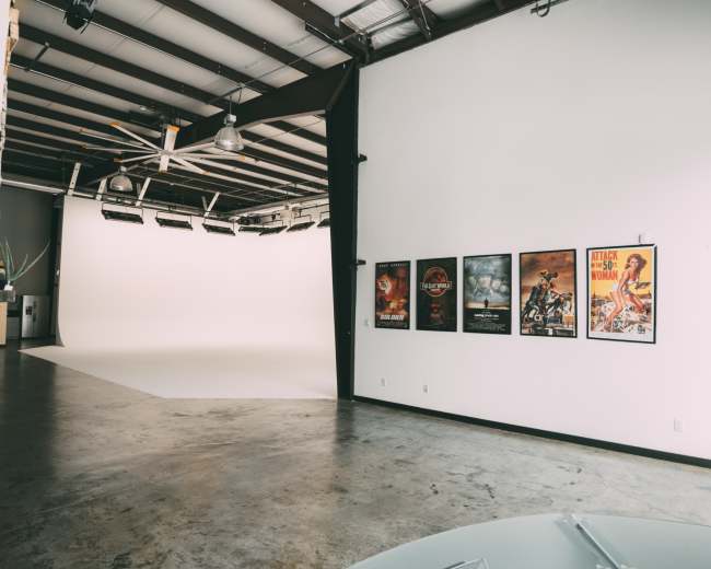 An industrial studio space with a white backdrop, polished concrete floor, and vintage movie posters hanging on the wall.