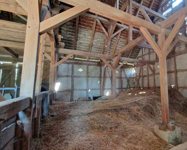 The image shows the interior of a barn with wooden beams and a large mound of straw on the floor.