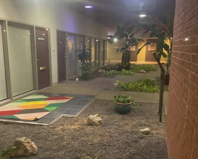 The image shows a corridor with several doorways, indoor plants, and a landscaped area featuring stones and greenery.